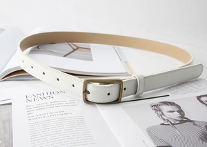 Detail of white leather belt featuring a vintage bronze rectangular buckle on magazines