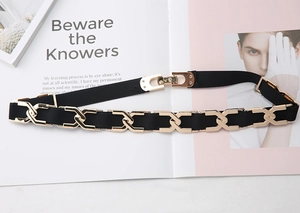 Détail d'une ceinture élastique noire avec chaîne dorée en forme de X et boucle en métal