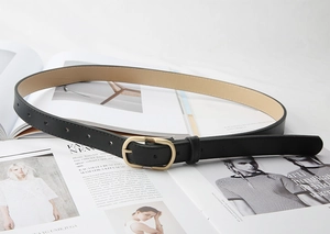 Detail of a thin black leather belt with a vintage gold oval buckle on a fashion magazine