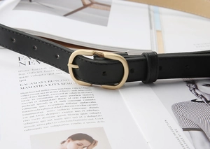 Close-up of black matte leather belt with pale gold oval buckle on a magazine background