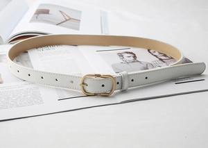 Detail view of a white leather belt with an oval matte gold buckle on fashion magazines