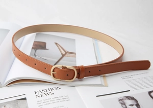 Detail of caramel faux leather belt with golden oval buckle on a fashion magazine