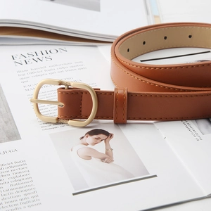 Classic brown leather belt for women with golden U-shaped buckle on a fashion magazine