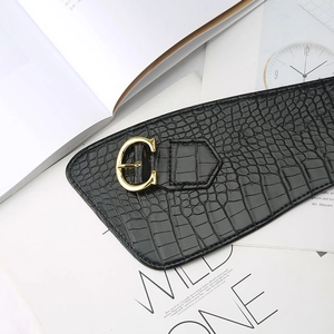 Detail of black faux leather wide belt with crocodile texture and gold C-shaped buckle