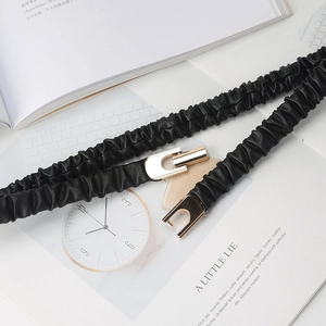 Detail view of black elastic waist belt with gold U-shaped buckle on lifestyle background