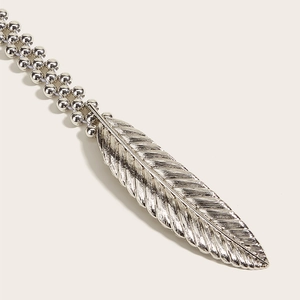 Macro shot of silver metal feather pendant with detailed texture and beaded waist chain