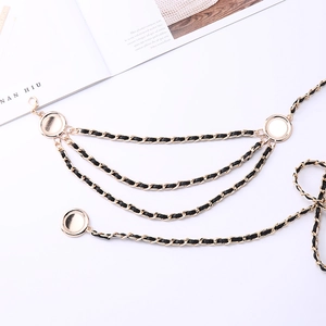 Detail of layered gold metal chain belt with black leather weave and round charms