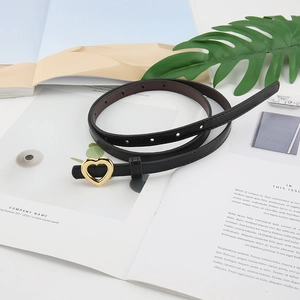 Détail d'une fine ceinture en cuir noir avec une boucle coeur dorée polie sur un magazine