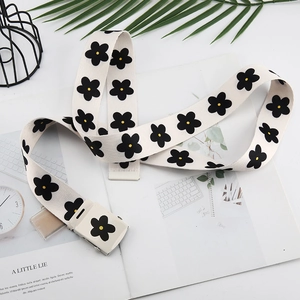 Détail de la ceinture en toile avec motif marguerite et boucle carrée en métal