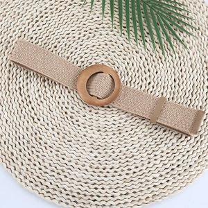 Detail of woven straw belt with a round wooden buckle on a natural spiral textured background