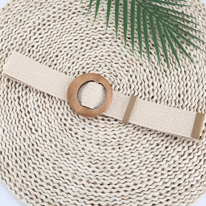 Detail of beige woven elastic belt featuring a round wooden buckle on a textured mat