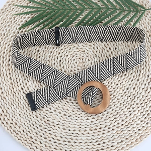 Detail of hand-woven geometric belt with natural round wooden buckle on textured background