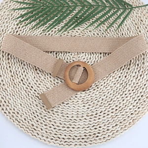Close-up of beige woven elastic belt with a round wooden buckle on a natural straw mat background