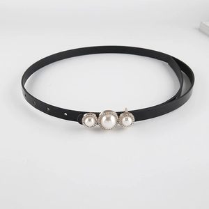 Détail d'une fine ceinture en cuir verni noir avec boucle dorée ornée de perles et strass