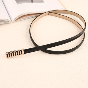 Gros plan d'une fine ceinture en cuir noir avec boucle dorée ondulée élégante sur fond