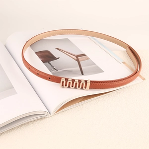 Ceinture fine en cuir marron pour femme avec boucle dorée ondulée sur un magazine