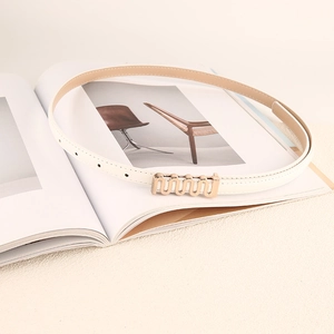 Gros plan sur une ceinture fine blanche avec boucle dorée ondulée sur un magazine