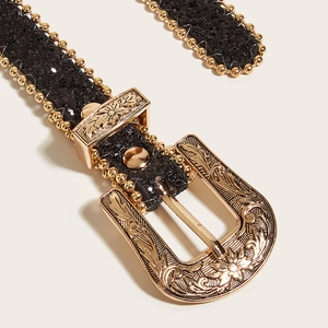 Détail de la boucle dorée gravée et ceinture pailletée noire avec bordures perlées