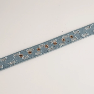 Dettaglio di una cintura in denim azzurro con occhielli metallici e toppe vintage