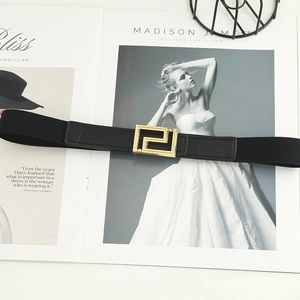 Elastic black waist belt with gold geometric buckle on a fashion magazine background