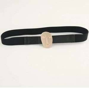 Detailed macro view of the black elastic belt featuring a golden abstract face metal buckle