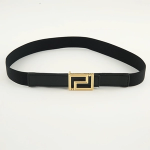 Detail view of black elastic belt featuring a decorative gold geometric G-shaped buckle