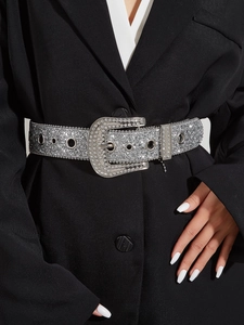 Gros plan d'une large ceinture argentée ornée de strass portée sur un blazer noir chic