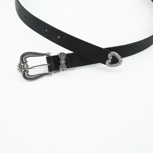 Detail view of thin black leather belt with retro floral silver buckle and heart tip