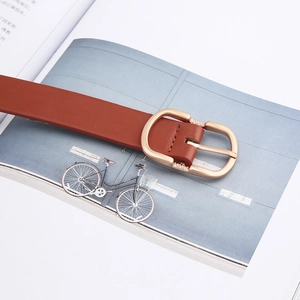 Detailed view of brown leather belt with unique gold metal buckle on a magazine background