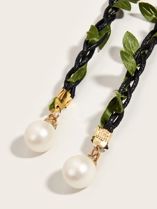 Detail of woven rope belt featuring green fabric leaves and pearl charms with rhinestones