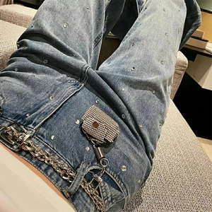 Detail of Y2K style denim jeans featuring rhinestone studs and silver metal chain belt with pouch