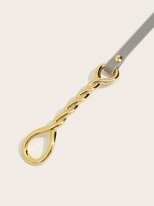 Detail of a slim gray leather belt with a polished golden twist-shaped buckle and rivet