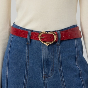 Détail d'une ceinture rouge texture crocodile avec boucle cœur dorée sur un jean bleu