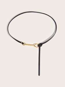 Detail of thin black leather belt featuring elegant gold metal knot and artistic link