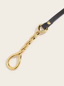 Detail of a thin black leather belt featuring a polished gold knot-shaped metal buckle