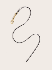 Detail of slim black leather belt with elegant golden spiral metal buckle on cream backdrop