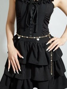 Détail d'une chaîne de taille dorée à perles avec pendentifs cœur sur robe noire