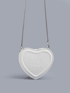 Close-up of white heart-shaped leather mini bag with embossed lettering and silver chain