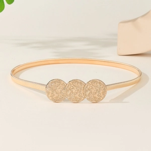 Elegant gold metal spring belt for dresses with textured circular buckle on beige background