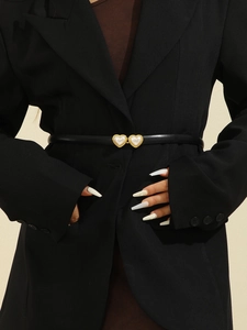Détail d'une ceinture fine en cuir verni noir avec boucle cœur dorée et insert en perle