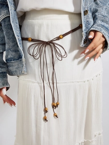 Gros plan sur la ceinture bohème tressée marron avec perles en bois sur robe blanche