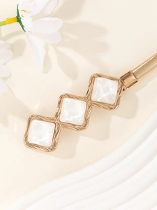 Close-up of golden elastic metal belt featuring white marble-pattern square inserts