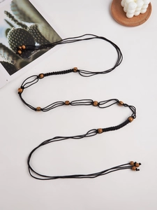 Détail d'une ceinture tressée noire style bohème Y2K avec perles en bois sur fond blanc