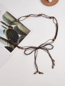 Détail d'une ceinture bohème tressée marron avec perles en bois clair et glands