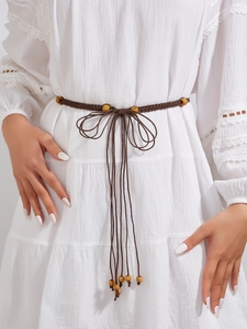 Détail d'une ceinture tressée bohème marron foncé avec perles en bois sur une robe blanche