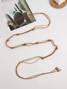 Détail de ceinture bohème tressée marron avec perles en bois sur fond blanc minimal