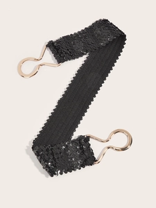 Detail of black sequined elastic belt showing golden metal hook closure on a flat surface