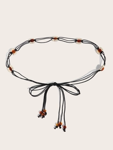 Détail d'une ceinture bohème tressée noire avec anneaux blancs et perles d'ambre