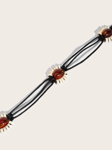 Détail d'une ceinture ethnique Y2K avec cordes noires tressées et perles en résine ambre