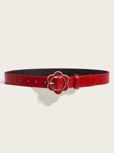 Close-up of red crocodile embossed belt featuring a silver floral buckle detail